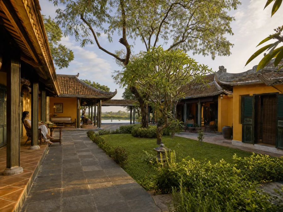 Bố cục làng biệt lập — ba khối nhà kết nối qua hành lang mái lá